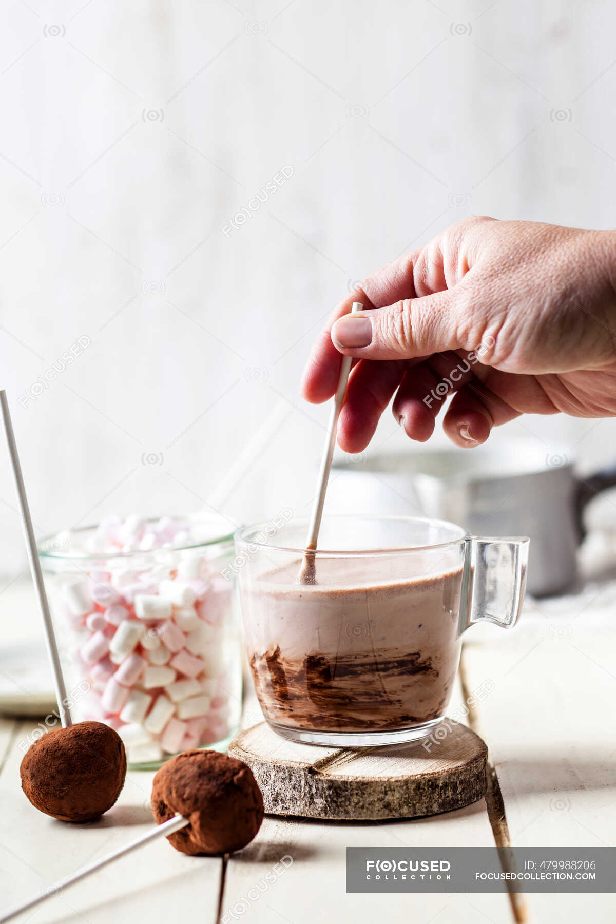 Hand of woman mixing hot chocolate by truffle lollipops and