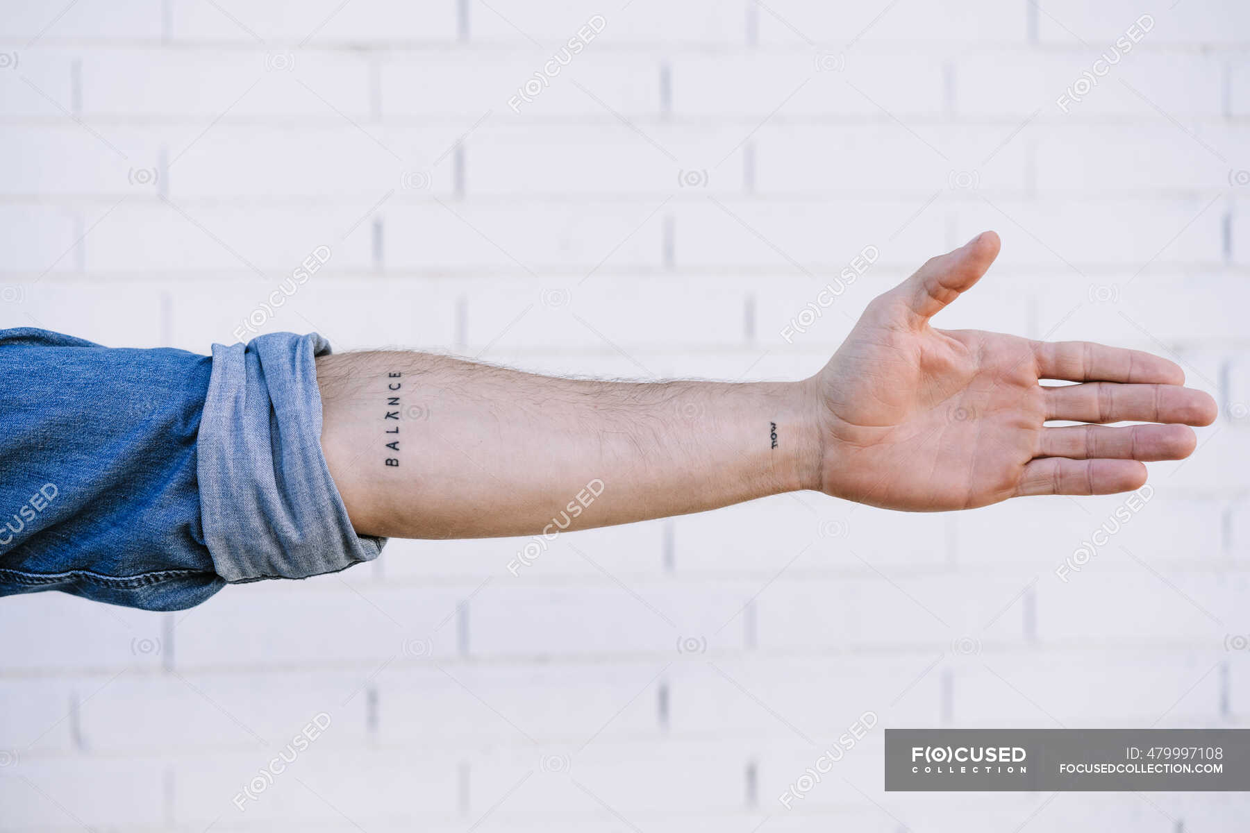 Young man with tattoo standing in front of brick wall with arms crossed  stock photo