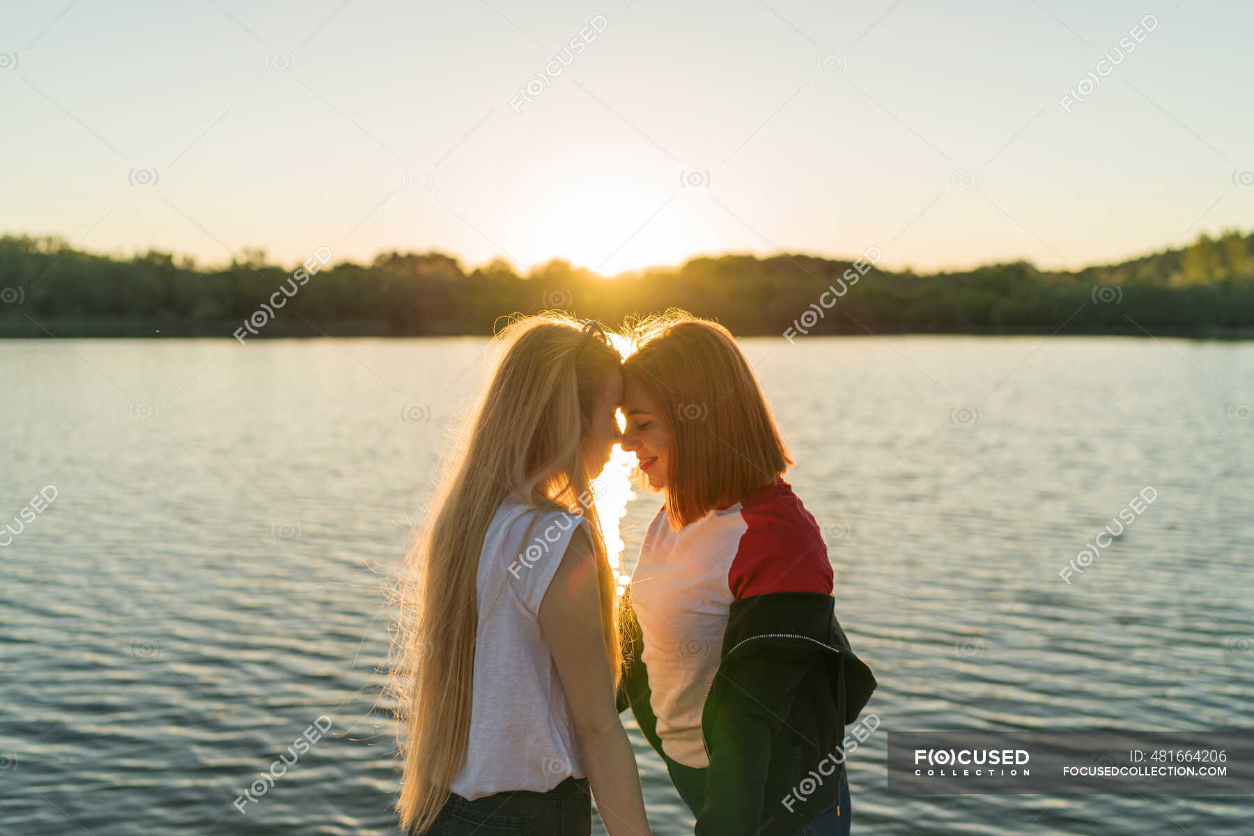 Lesbian Couple Standing Face To Face While Standing Against Lake During Sunset — Outdoors