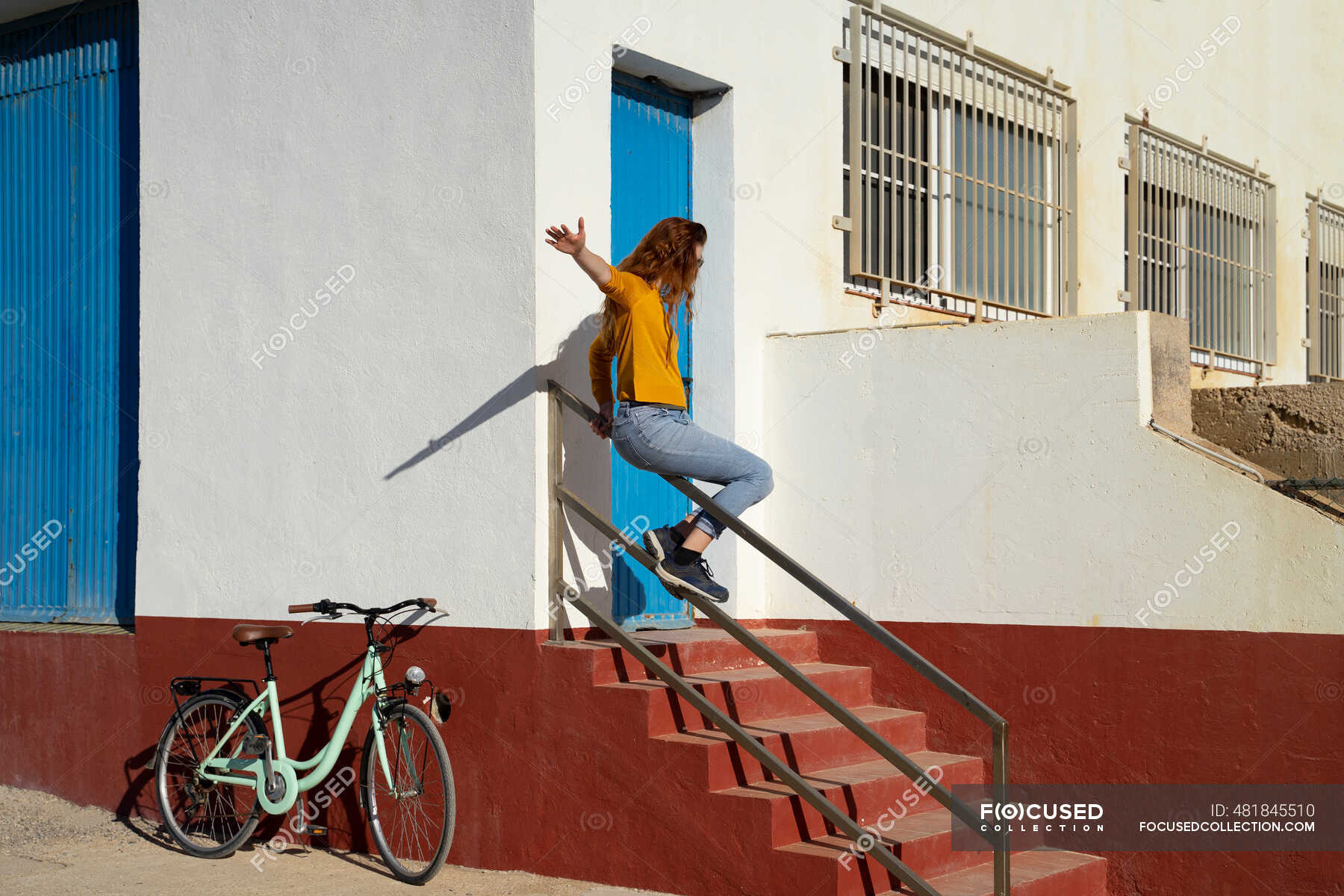 Young woman sliding on railing by white built structure during sunny day — fun, bicycle Stock