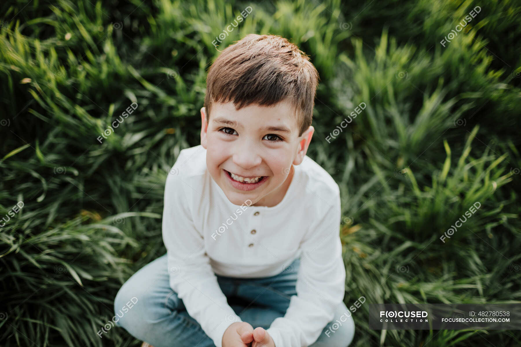 playful-boy-sitting-cross-legged-on-grass-innocence-toddlers-stock