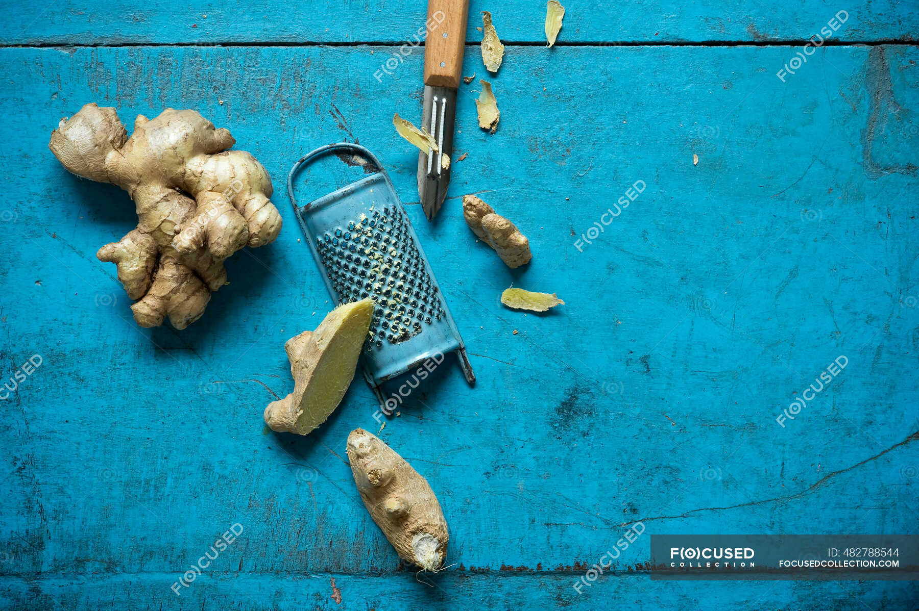 Ginger root, grater and kitchen knife lying on blue wooden surface