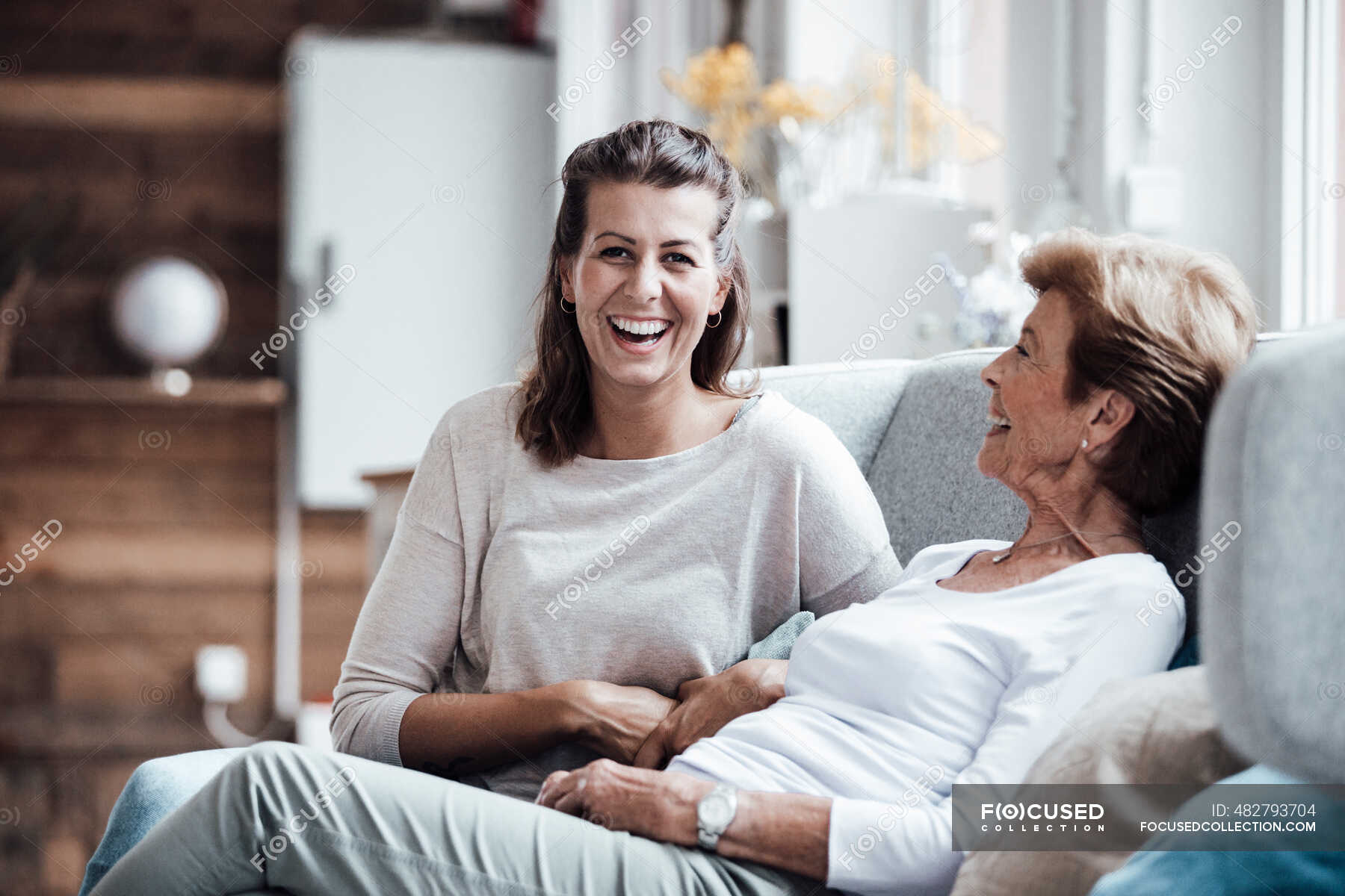 Laughing woman sitting by grandmother on sofa at home — indoors, Adult ...