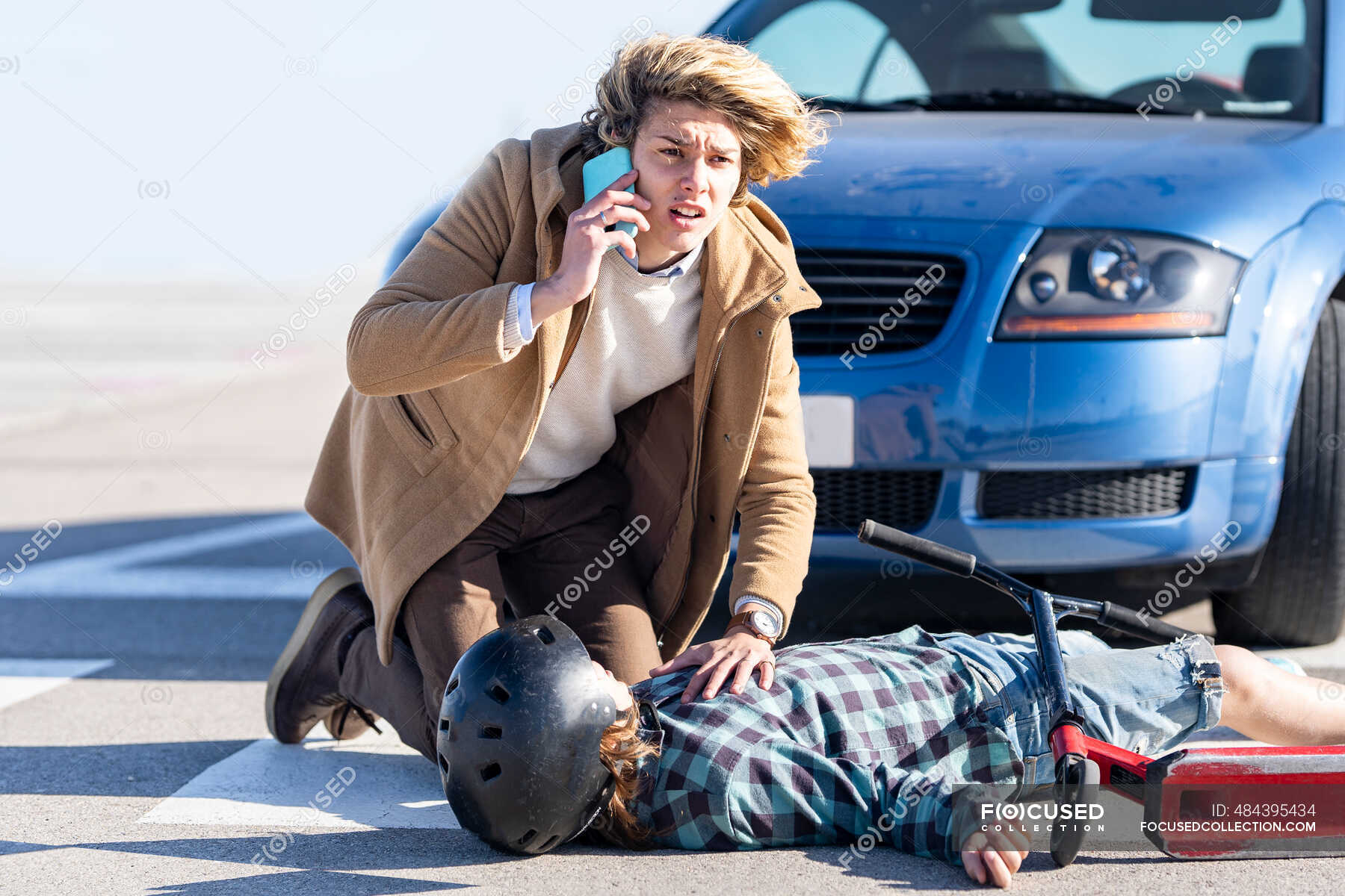 Young man calling help on mobile phone with boy in background lying on road  after car accident — spain, outdoors - Stock Photo | #484395434