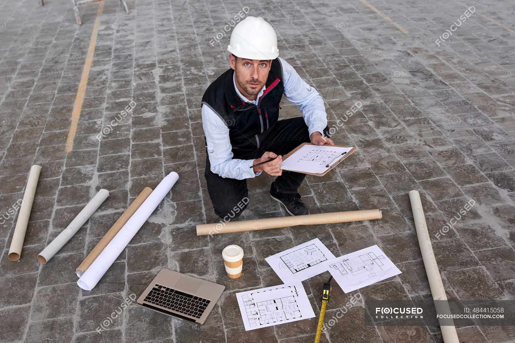 male-engineer-holding-site-plan-while-kneeling-on-floor-in-building