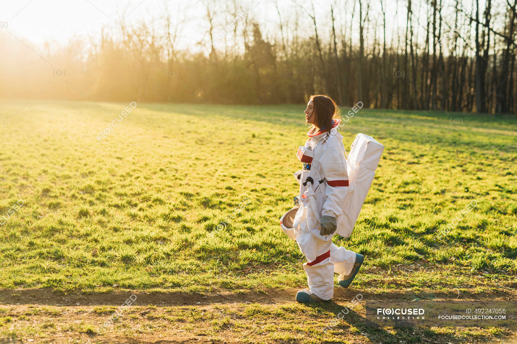 female-astronaut-in-space-suit-walking-by-grass-land-on-sunny-day