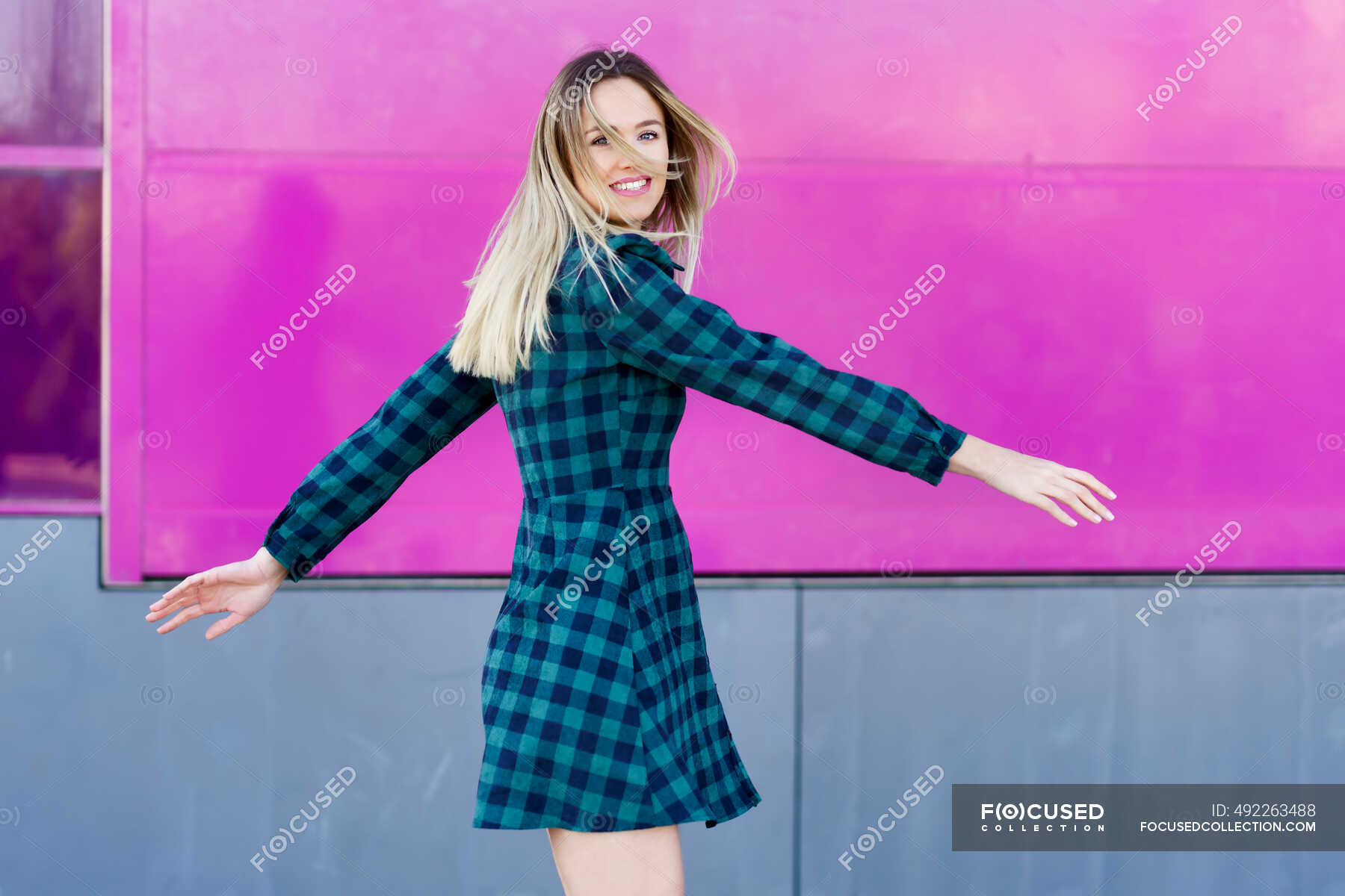 smiling-woman-with-arms-outstretched-standing-by-pink-wall-long-hair