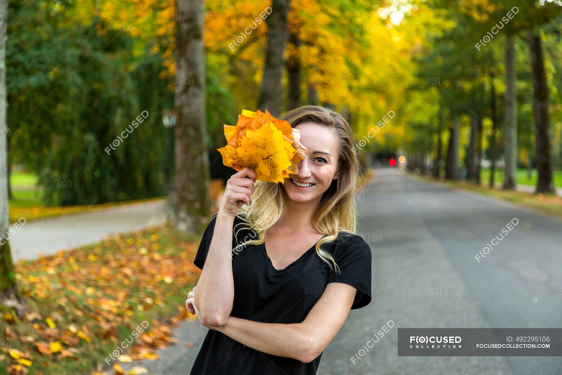 Portrait of laughing woman with bunch of autumn leaves on avenue ...