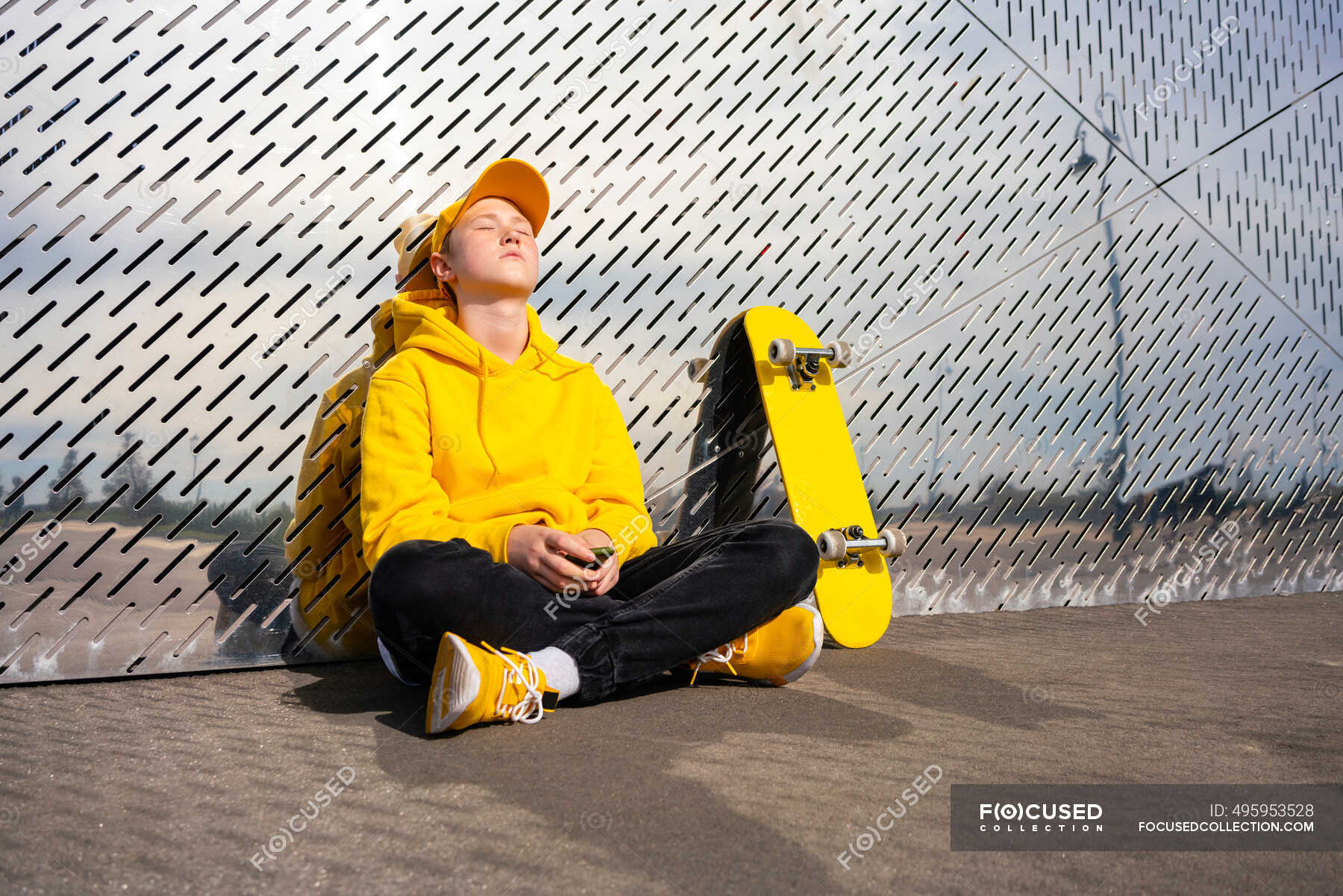 sad-boy-sitting-cross-legged-while-resting-at-metal-wall-mobile-phone