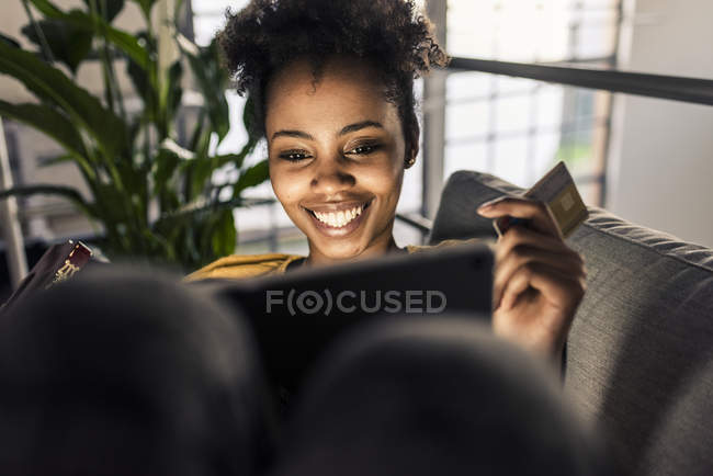 Smiling young woman sitting on couch with credit card and laptop — Stock Photo