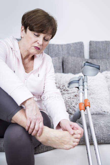 Senior woman with crutches sitting on couch — Stock Photo