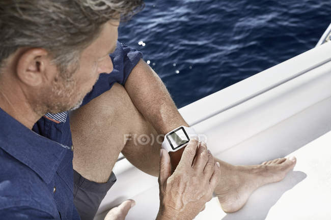 Uomo seduto su uno yacht a guardare smartwatch — Foto stock