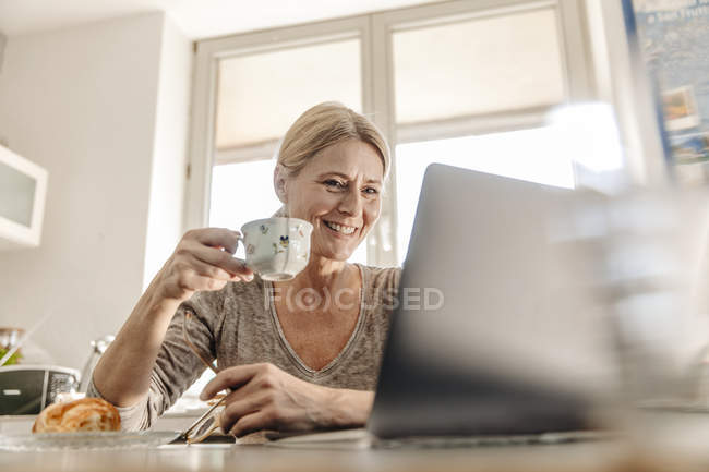 Woman having breakfast and using laptop — Stock Photo
