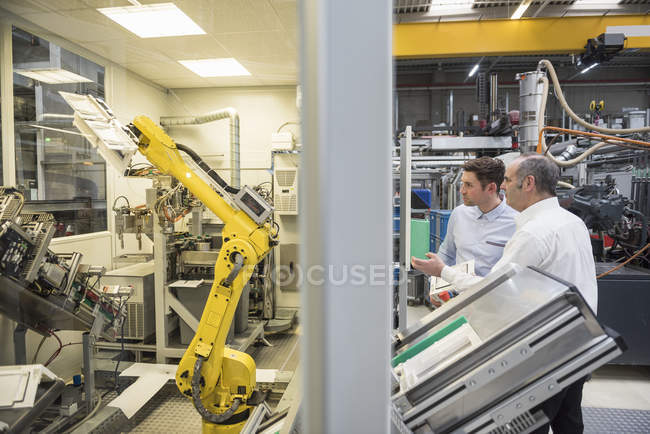Hombres que examinan robot industrial - foto de stock