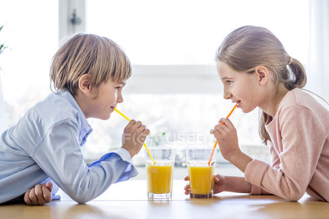 Hermano y hermana bebiendo jugo de naranja - foto de stock