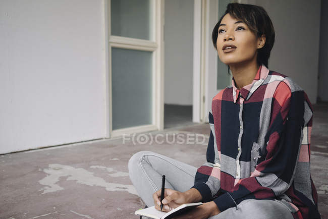 Жінка сидить на тріснутій підлозі з блокнотом — стокове фото