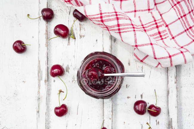 Cherries beside open jar of cherry jam — Stock Photo