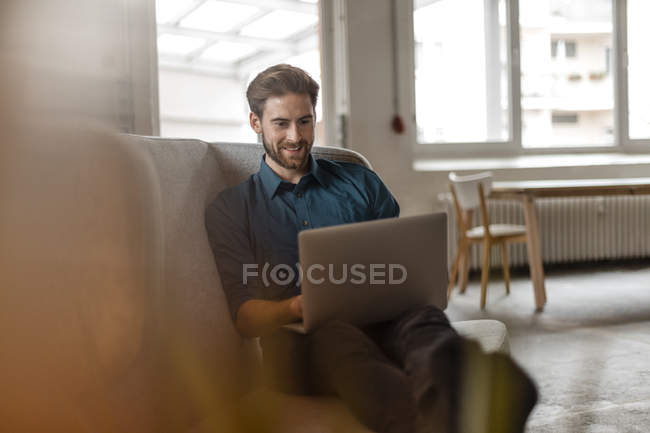 Freiberufler sitzt auf Couch und nutzt Laptop — Stockfoto