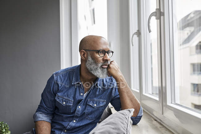 Hombre maduro sentado en la ventana, mirando preocupado - foto de stock