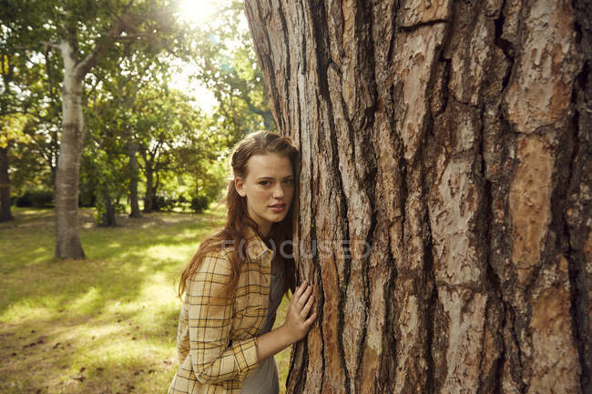 Mujer apoyada en tronco de árbol - foto de stock