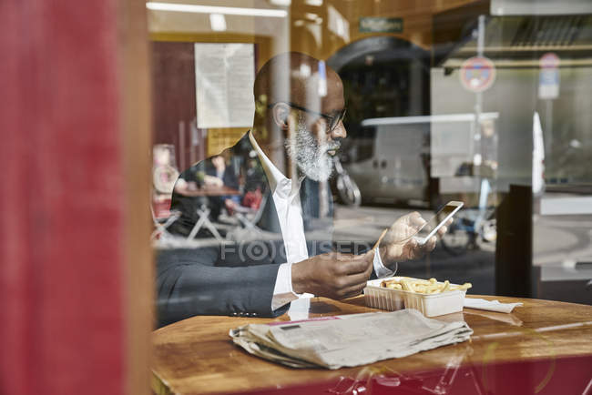 Geschäftsmann in Imbiss schaut aufs Smartphone — Stockfoto