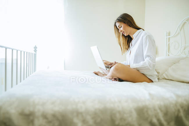 Woman sitting on bed using laptop — Stock Photo