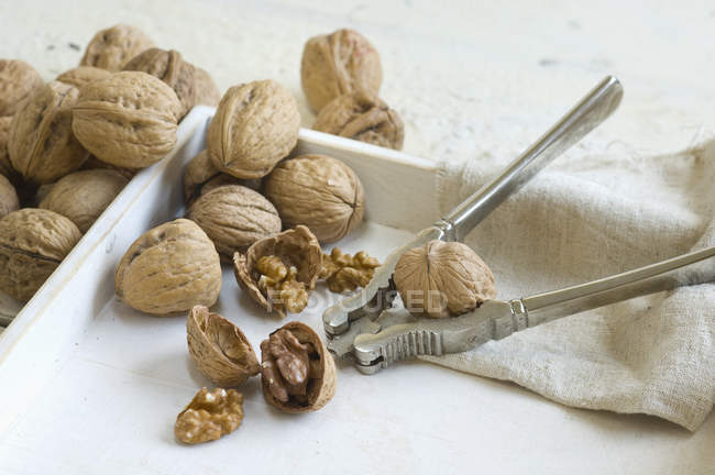 Whole and cracked walnuts and nutcracker on tray — Stock Photo