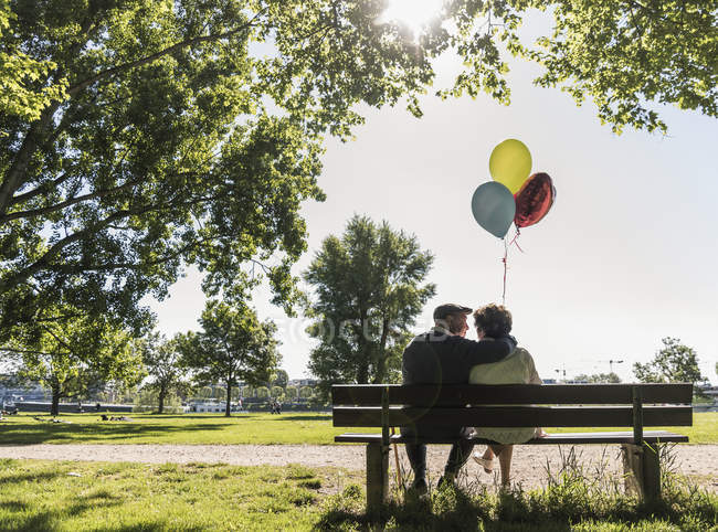 Coppia senior con palloncini che si abbracciano in panchina — Foto stock