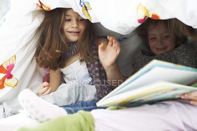 Children with book under blanket — Stock Photo