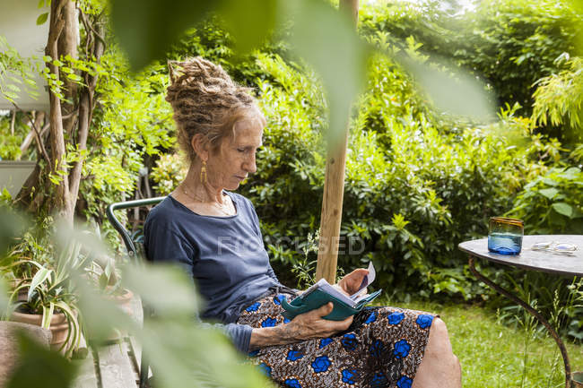 Senior woman with dreadlocks sitting in the garden looking at personal organizer — Stock Photo