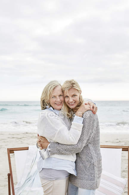 Madre e hija abrazándose en la playa - foto de stock