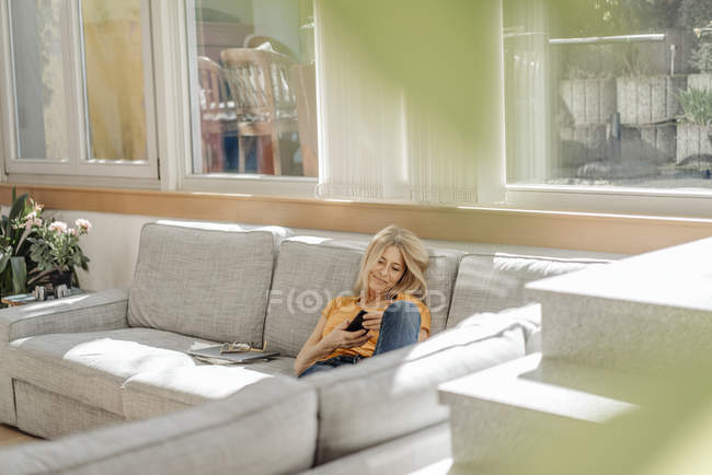 Mujer en el sofá usando el teléfono celular - foto de stock