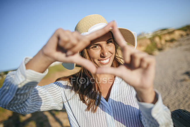 Mujer haciendo marco de dedo en la playa - foto de stock