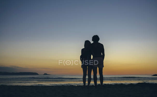 Jeune couple regardant coucher de soleil sur la plage — Photo de stock