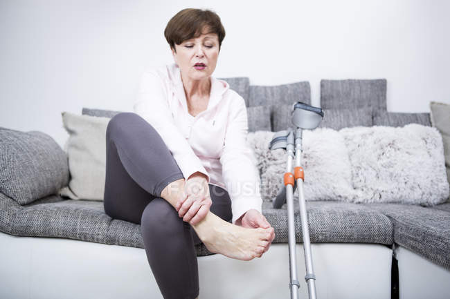 Donna anziana controllo caviglia sul divano — Foto stock