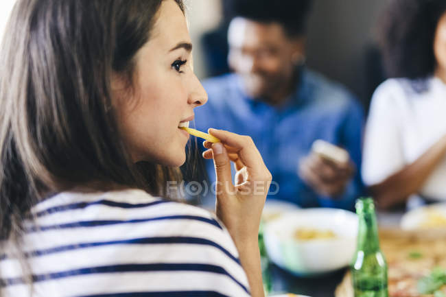 Mulher jovem comendo batata frita assistindo filme na mesa azul