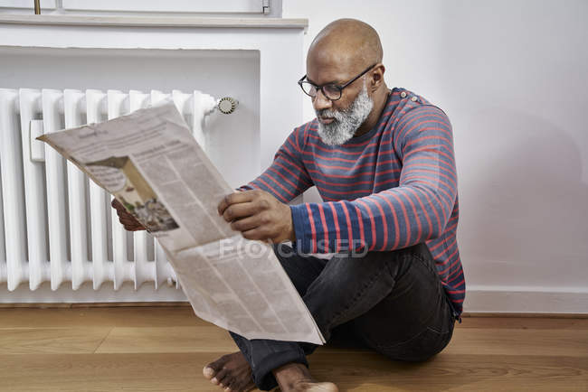 Man sitting on floor and reading newspaper — Stock Photo