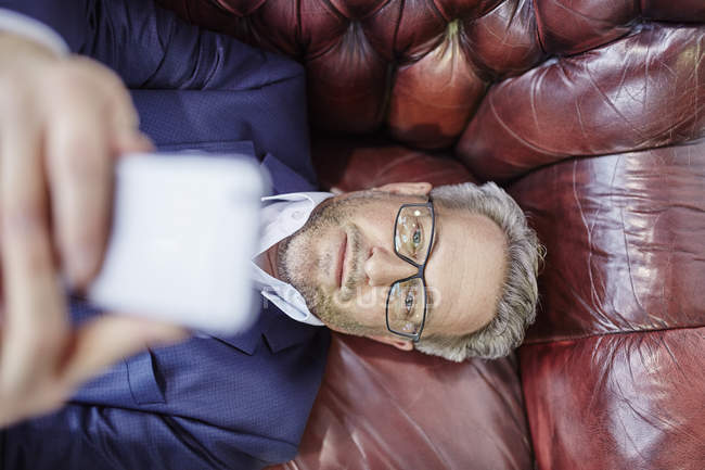 Geschäftsmann legt sich hin und schaut aufs Handy — Stockfoto