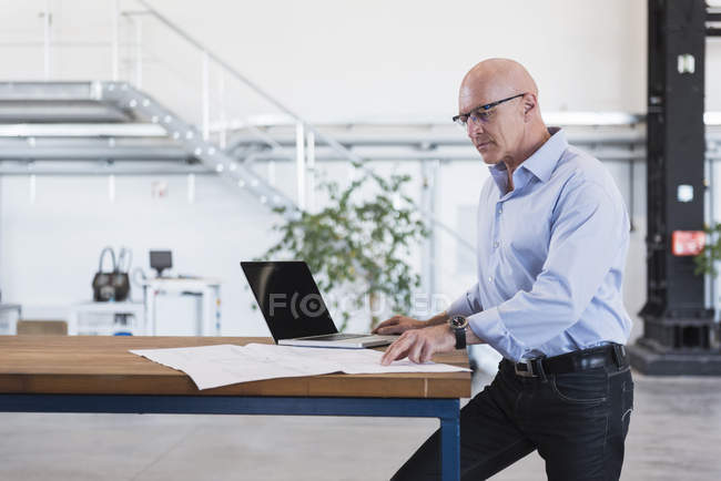 Hombre usando el ordenador portátil con el plan en la mesa - foto de stock