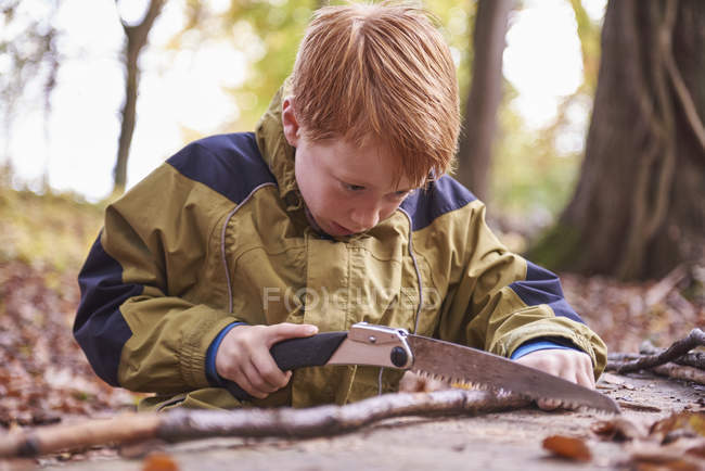 Рыжий мальчик рубит деревянную ветку ножом, вид крупным планом — стоковое фото