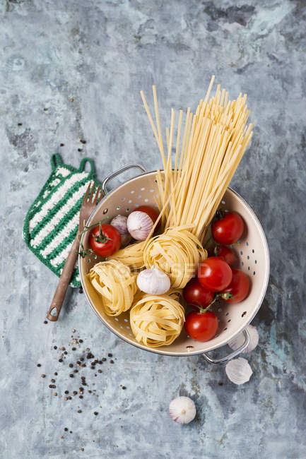 Spaghetti, pomodori e bulbi di aglio nel colino — Foto stock