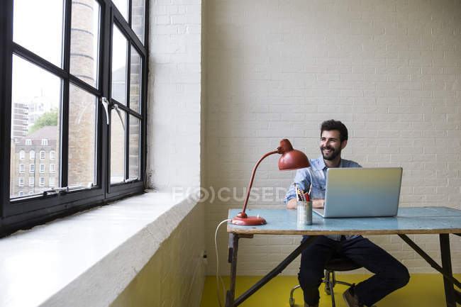Smiling man sitting at desk with laptop — Stock Photo