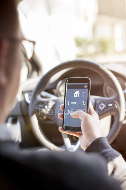 Man in car adjusting devices at home via smartphone — Stock Photo