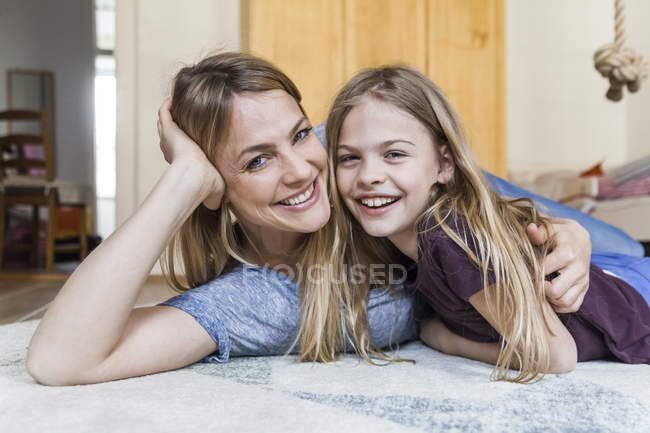 Porträt eines glücklichen Mädchens, das mit seiner Mutter auf dem Boden liegt — Stockfoto
