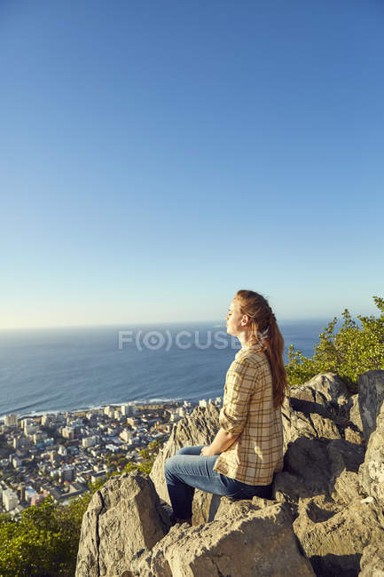 Woman sitting on rock with view to city — Stock Photo