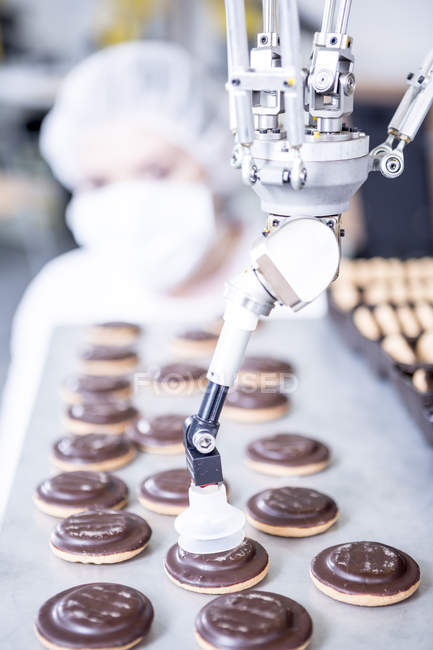 Robot handling cookies with woman in background — Stock Photo