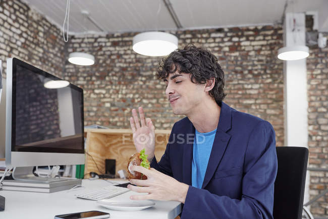 Человек ест сэндвич в офисе — стоковое фото