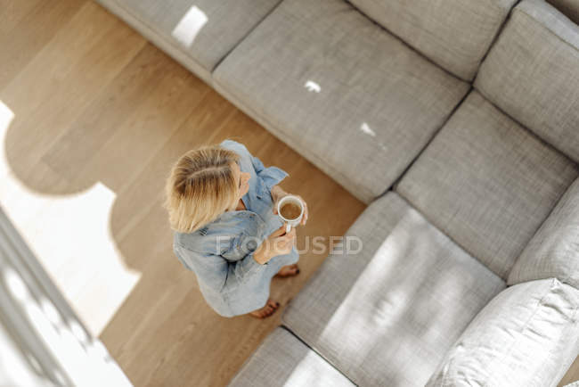 Frau im Wohnzimmer mit Tasse Kaffee — Stockfoto