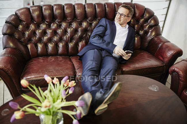 Geschäftsmann hält Handy auf Couch — Stockfoto