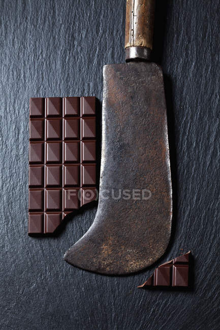 Chocolate bar and rusty cleaver on slate — Stock Photo